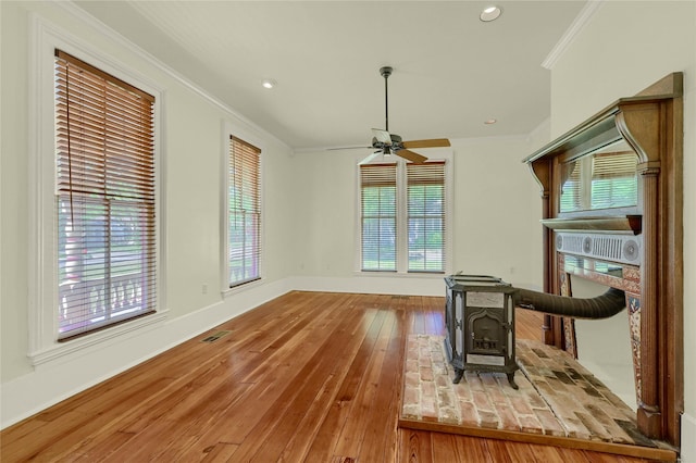 living area with a wood stove, visible vents, crown molding, hardwood / wood-style flooring, and ceiling fan