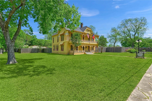 rear view of house featuring a fenced backyard, a chimney, a balcony, and a lawn