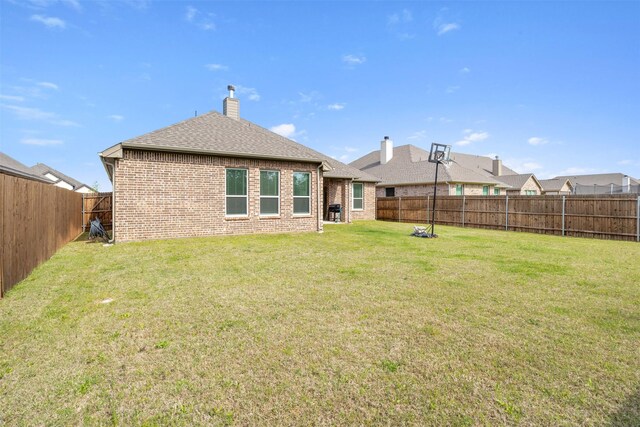 back of property with a chimney, a fenced backyard, roof with shingles, a lawn, and brick siding