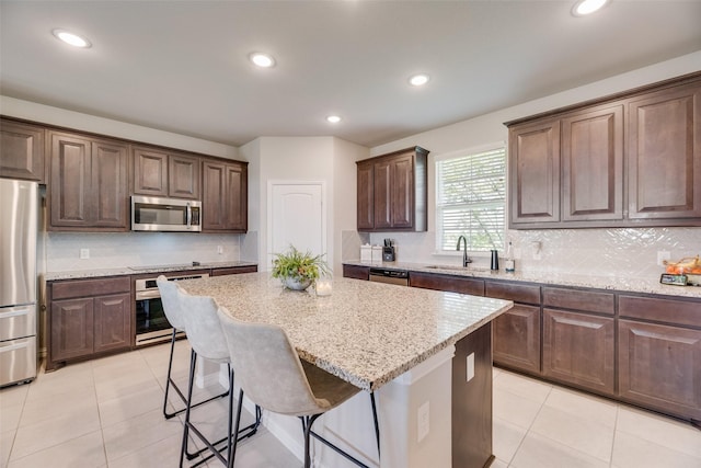 kitchen with stainless steel appliances, a center island, a kitchen breakfast bar, a sink, and light stone countertops