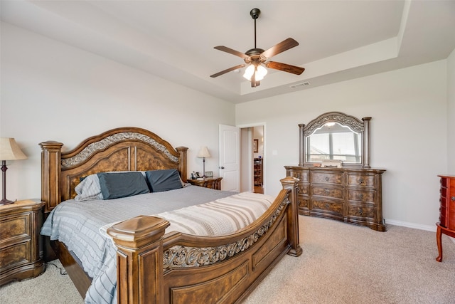 bedroom with a tray ceiling, baseboards, visible vents, light colored carpet, and a ceiling fan