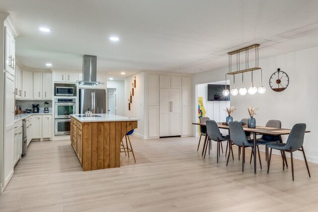 4043 Flintridge Dr, Dallas, TX 75244 - kitchen with island exhaust hood, an island with sink, stainless steel appliances, light countertops, and light wood-type flooring
