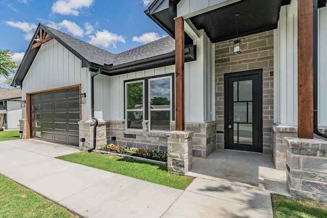 doorway to property featuring board and batten siding, an attached garage, driveway, stone siding, and roof with shingles