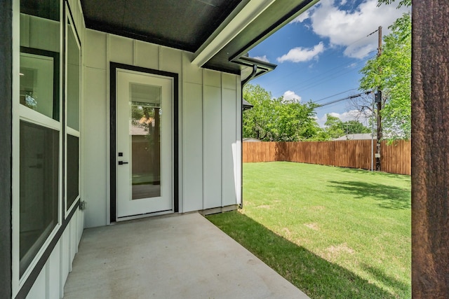 entrance to property with board and batten siding, a patio area, fence, and a yard