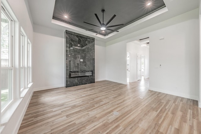 unfurnished living room featuring a ceiling fan, a healthy amount of sunlight, wood finished floors, and a raised ceiling