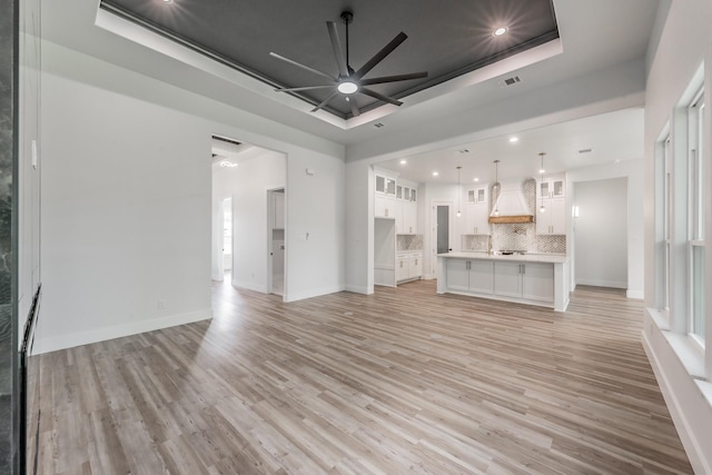 unfurnished living room featuring ceiling fan, a tray ceiling, light wood-style flooring, visible vents, and recessed lighting