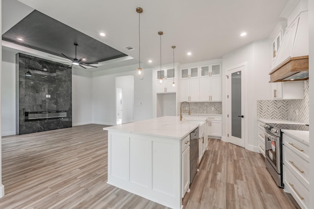 kitchen featuring light wood finished floors, tasteful backsplash, a ceiling fan, custom range hood, and appliances with stainless steel finishes