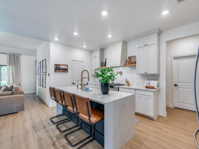 kitchen with white cabinets, light wood finished floors, stainless steel dishwasher, a sink, and hanging light fixtures