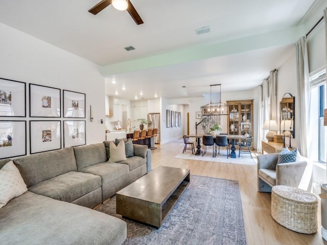 living room featuring light wood finished floors, a glass covered fireplace, visible vents, and ceiling fan