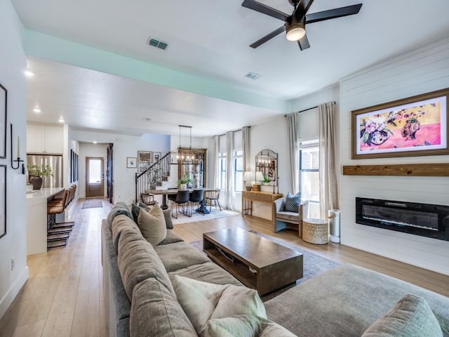 living room with light wood-style flooring, visible vents, baseboards, and ceiling fan with notable chandelier