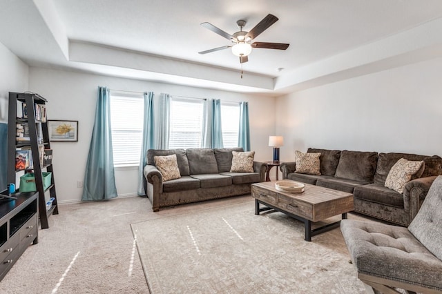 living room featuring baseboards, ceiling fan, light carpet, and a tray ceiling