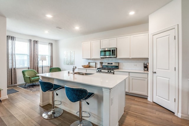 kitchen with a sink, a kitchen breakfast bar, an island with sink, stainless steel appliances, and decorative backsplash