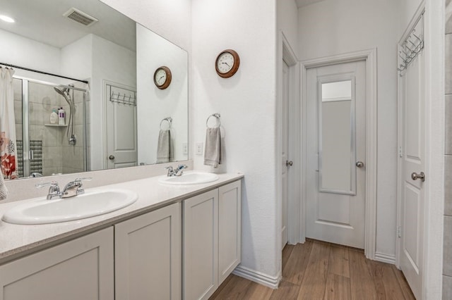 full bathroom with visible vents, a sink, wood finished floors, and tiled shower