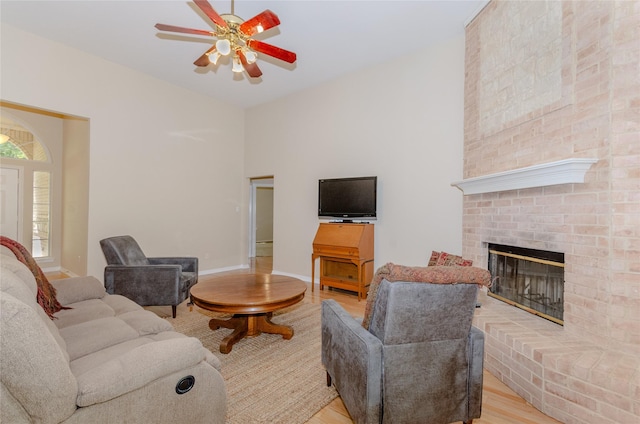 living area with a fireplace, light wood-type flooring, a ceiling fan, and baseboards