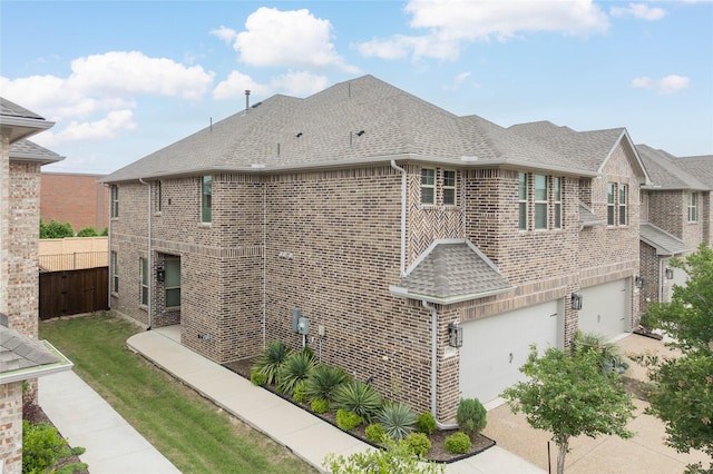 view of property exterior featuring brick siding, an attached garage, roof with shingles, and fence