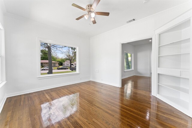 unfurnished room with crown molding, wood finished floors, ceiling fan, built in features, and visible vents