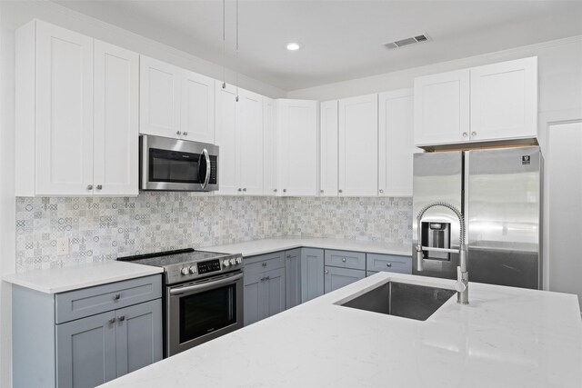 kitchen featuring light stone counters, gray cabinets, stainless steel appliances, and a sink
