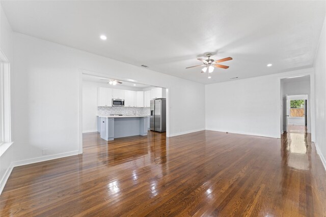 unfurnished living room with dark wood-type flooring, baseboards, and ceiling fan