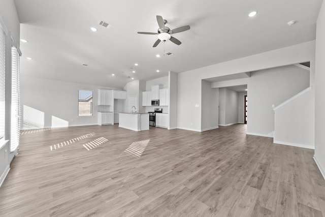 unfurnished living room featuring vaulted ceiling, visible vents, a ceiling fan, a sink, and baseboards