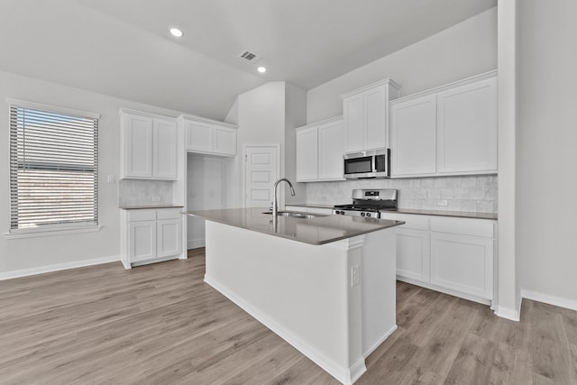 kitchen with vaulted ceiling, a sink, a kitchen island with sink, stainless steel appliances, and visible vents