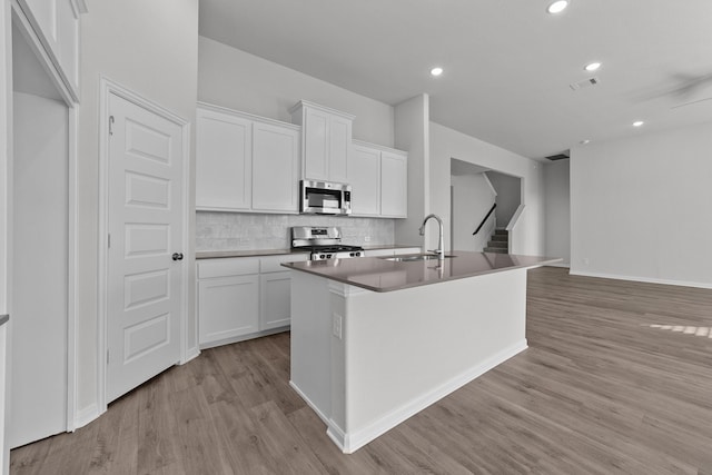kitchen featuring light wood finished floors, stainless steel appliances, a sink, a kitchen island with sink, and tasteful backsplash