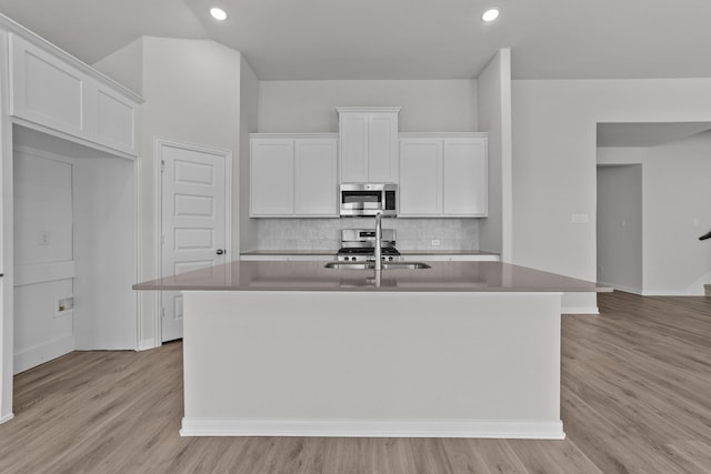 kitchen with white cabinets, a sink, a center island with sink, tasteful backsplash, and appliances with stainless steel finishes