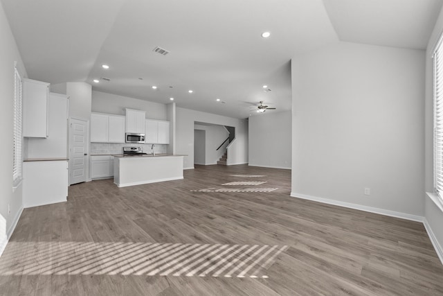unfurnished living room with lofted ceiling, stairs, visible vents, and recessed lighting