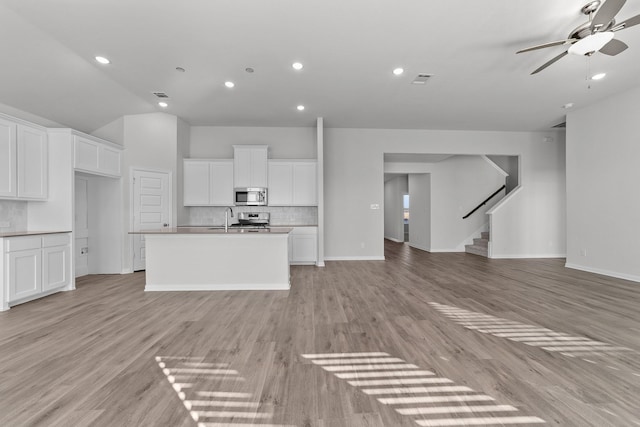 unfurnished living room featuring stairway, a sink, light wood-style floors, ceiling fan, and baseboards