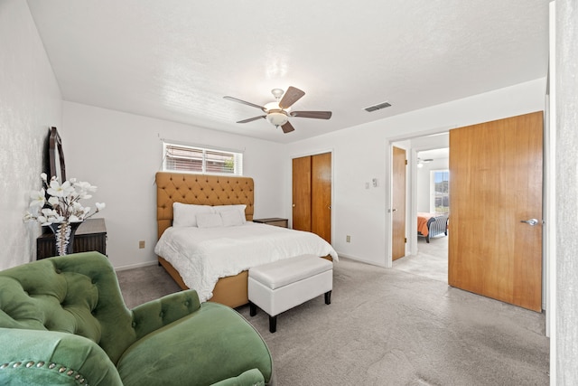 bedroom featuring ceiling fan, visible vents, light carpet, and multiple windows