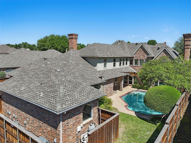 rear view of house featuring brick siding, a fenced backyard, a shingled roof, and a chimney