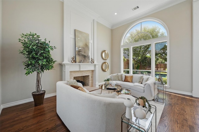 living room with dark wood-style flooring, baseboards, visible vents, a fireplace with raised hearth, and crown molding
