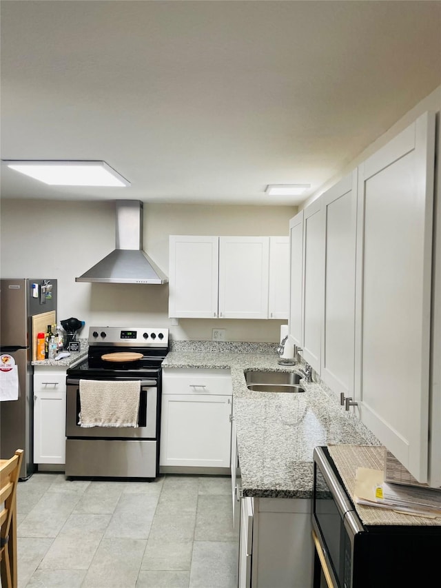 kitchen with light stone countertops, wall chimney range hood, white cabinets, a sink, and appliances with stainless steel finishes