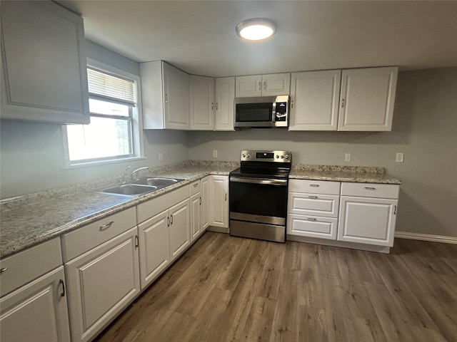 kitchen with stainless steel appliances, light countertops, wood finished floors, a sink, and white cabinetry