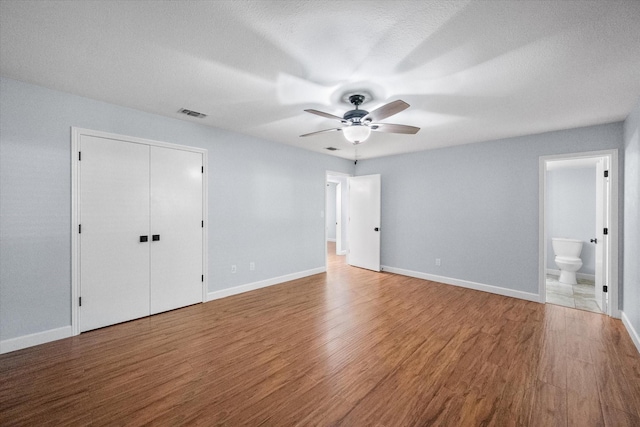 unfurnished bedroom with baseboards, wood finished floors, visible vents, and ensuite bathroom