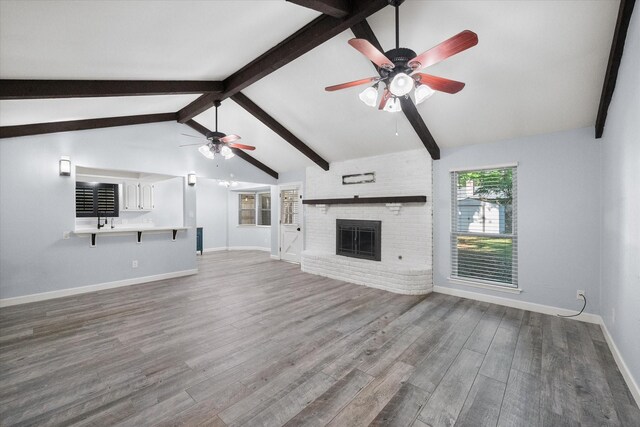 unfurnished living room with wood finished floors, vaulted ceiling with beams, ceiling fan, baseboards, and a brick fireplace