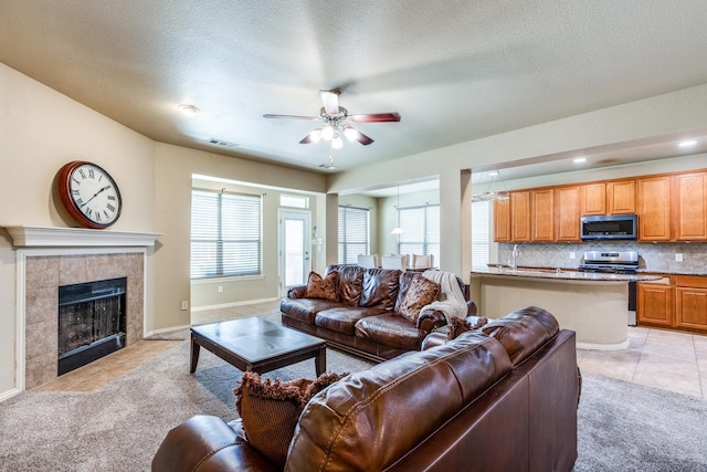 10625 Sexton Dr, Mckinney, TX 75072 - living room with light carpet, a ceiling fan, a tiled fireplace, a textured ceiling, and light tile patterned floors