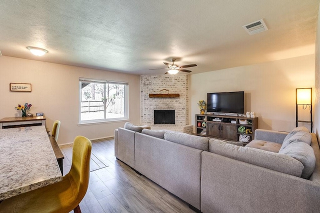 living area featuring wood finished floors, ceiling fan, baseboards, a brick fireplace, and visible vents