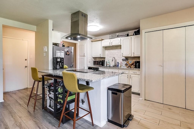 kitchen with a kitchen breakfast bar, island range hood, light wood-type flooring, appliances with stainless steel finishes, and white cabinetry