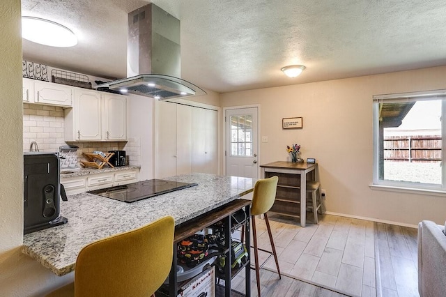 kitchen with island range hood, black electric stovetop, a kitchen breakfast bar, and a wealth of natural light