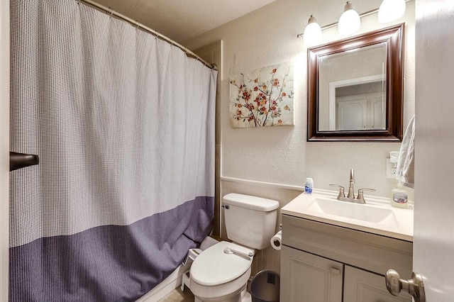 full bathroom featuring wainscoting, vanity, a textured wall, a shower with curtain, and toilet