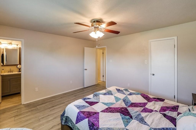 bedroom featuring light wood finished floors, a sink, baseboards, ceiling fan, and ensuite bath