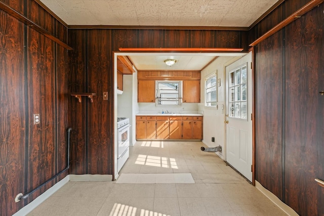 kitchen with white range with gas cooktop, light countertops, wood walls, and a sink