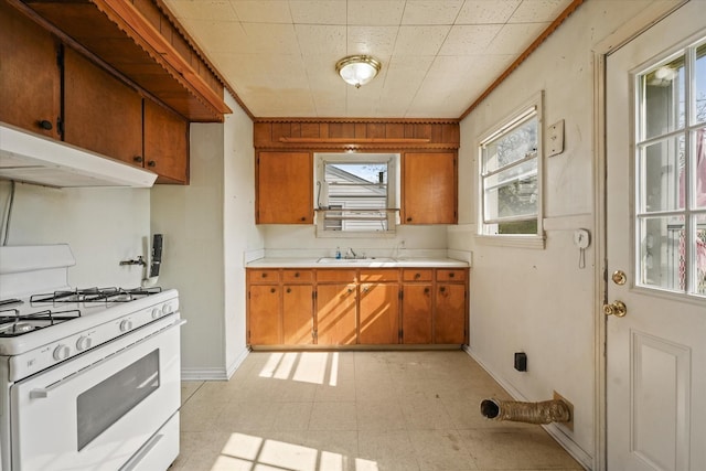 kitchen with white gas range, a sink, brown cabinetry, light floors, and light countertops
