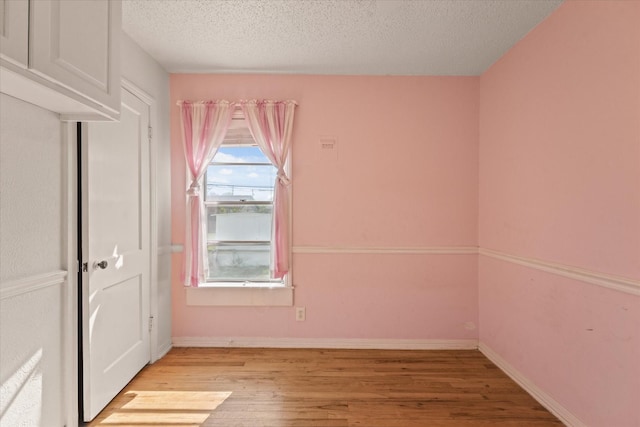 unfurnished room featuring baseboards, a textured ceiling, and light wood finished floors