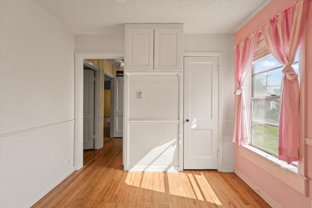 unfurnished bedroom with a textured ceiling, light wood finished floors, and baseboards