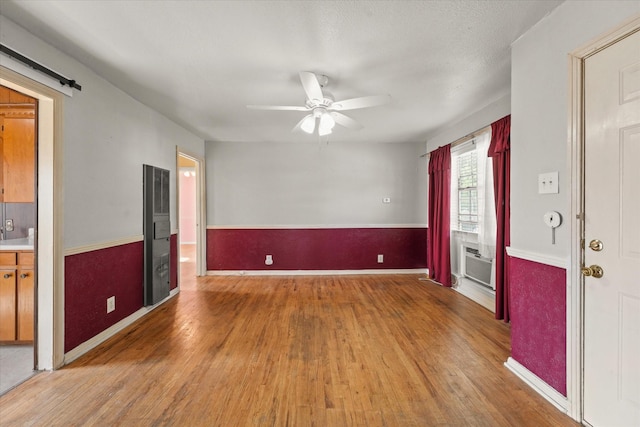 unfurnished room featuring cooling unit, a ceiling fan, wood finished floors, and a barn door