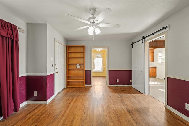 spare room with a barn door, wood finished floors, a ceiling fan, and baseboards