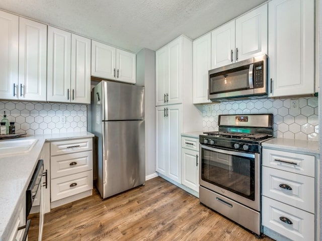 2631 Greenhurst Dr, Farmers Branch, TX 75234 - kitchen with appliances with stainless steel finishes, light countertops, light wood-type flooring, white cabinets, and a textured ceiling