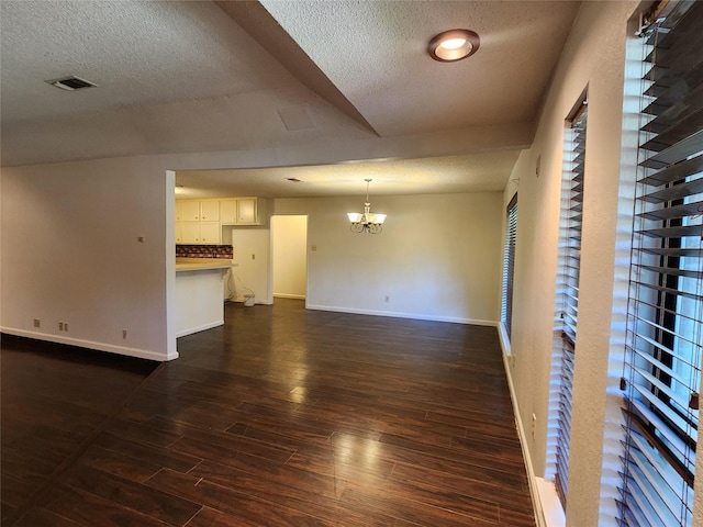 unfurnished living room with dark wood-style floors, a textured ceiling, baseboards, and an inviting chandelier