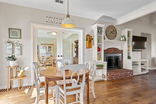 dining room with visible vents, a ceiling fan, wood finished floors, crown molding, and a fireplace